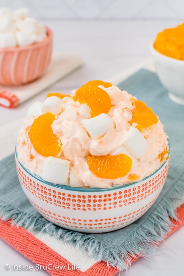 A bowl of Orange Creamsicle Fluff topped with oranges and marshmallows on a blue towel.