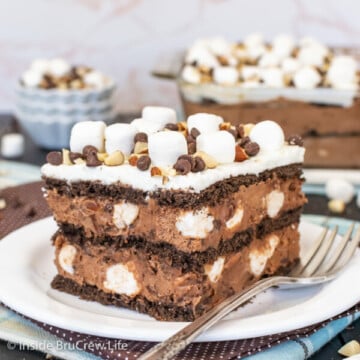 A white plate with a square of chocolate icebox cake topped with marshmallows, nuts, and chocolate chips on it.