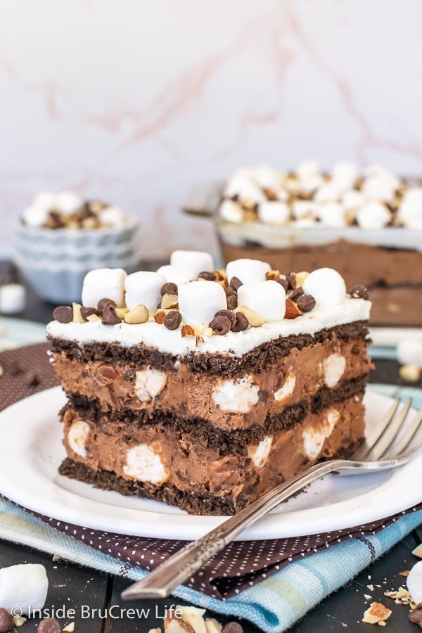 A white plate with a square of chocolate icebox cake topped with marshmallows and nuts on it.