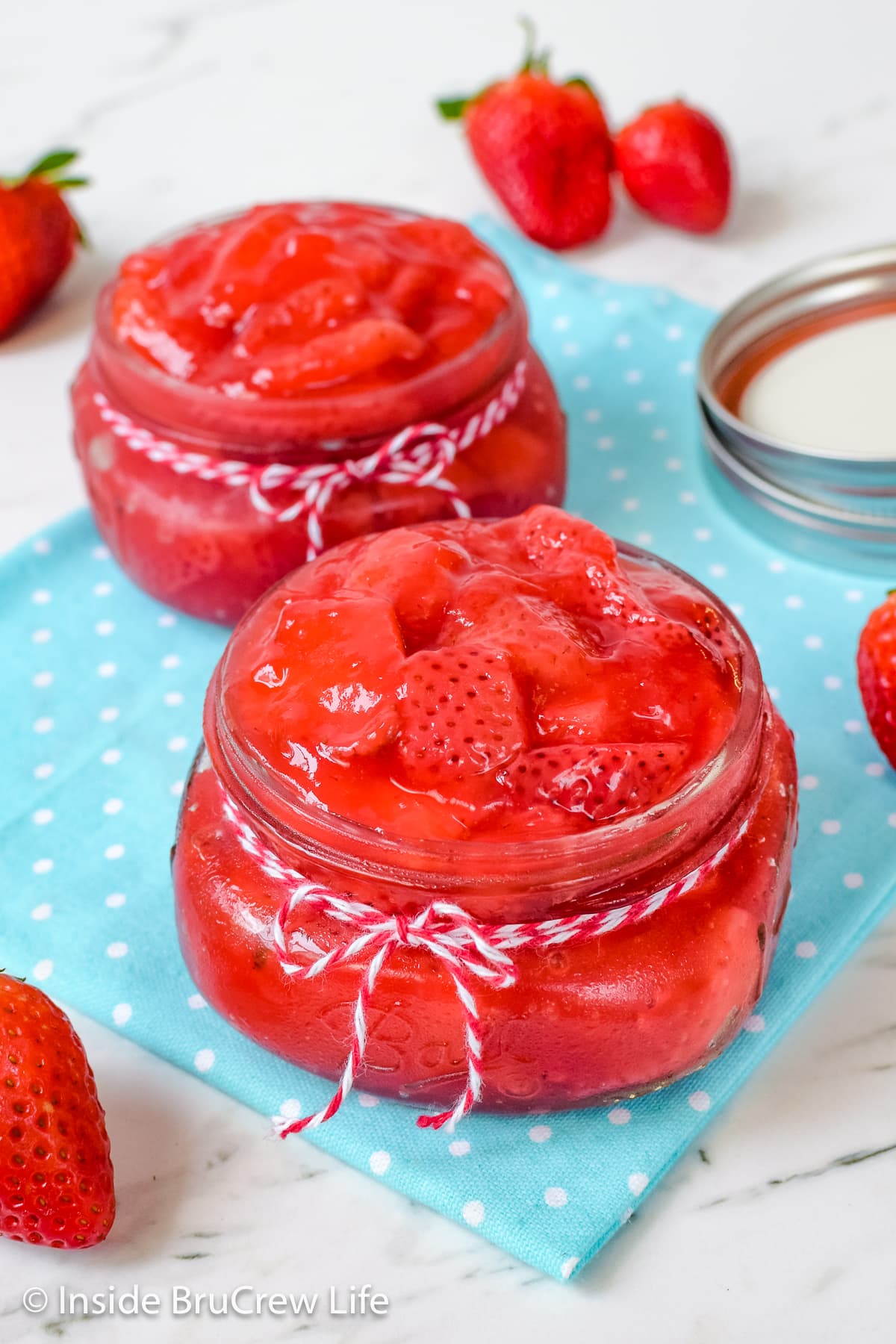 Strawberry pie filling inside two clear jars on a blue towel.