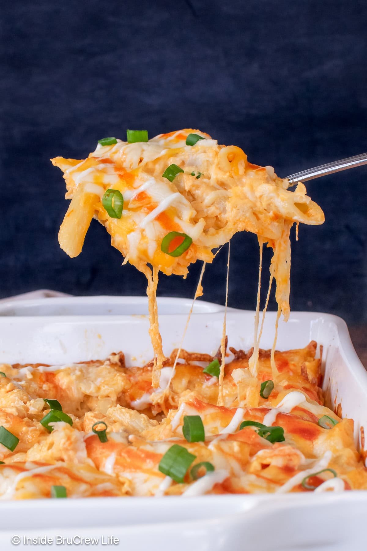 A scoop of cheesy pasta being lifted out of a casserole dish.