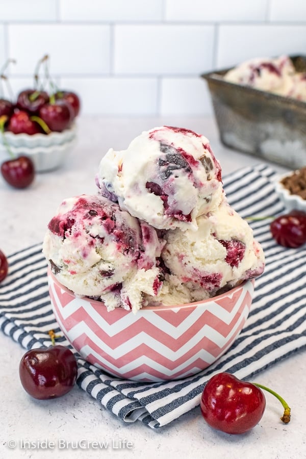 A pink and white bowl on a white board filled with three large scoops of cherry vanilla ice cream.