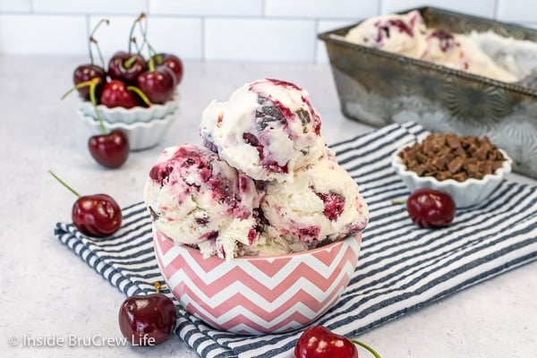 A pink and white bowl filled with scoops of vanilla ice cream loaded with cherry pie filling and chocolate chunks.