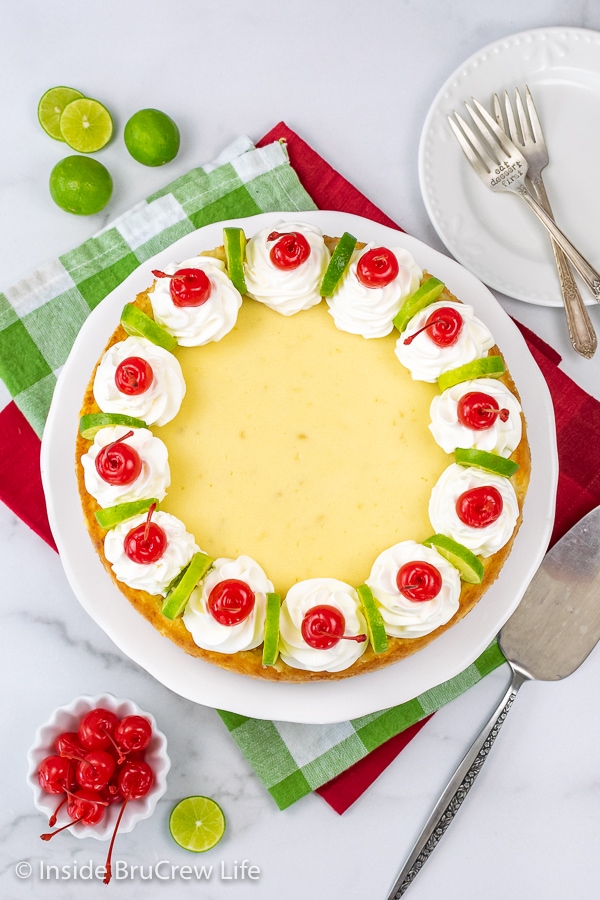 Overhead picture of the top of a key lime cheesecake that is decorated with whipped cream, lime slices, and maraschino cherries.