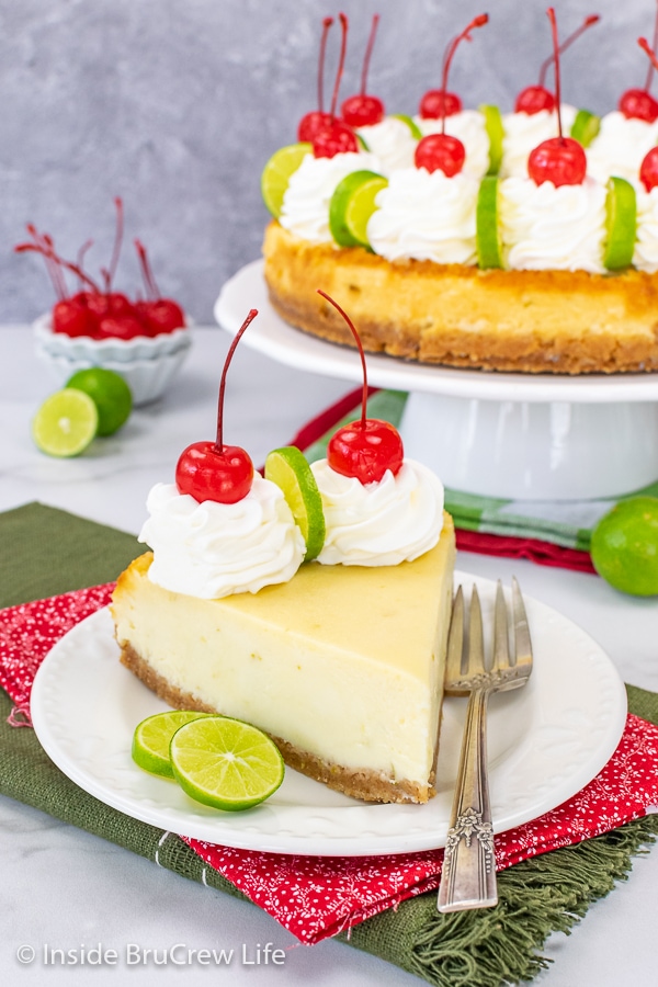 A white plate with a slice of key lime cheesecake on it and a plate with the rest of the cheesecake behind it.