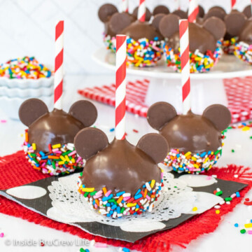 Three mickey mouse cake pops dipped in chocolate and colorful sprinkles with red and white straws.