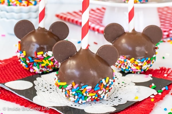 Three Mickey Mouse cake pops dipped in chocolate and sprinkles with a red and white straw in the tops.