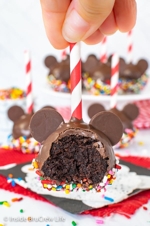 A hand holding a Mickey cake pop in the air missing a bite.
