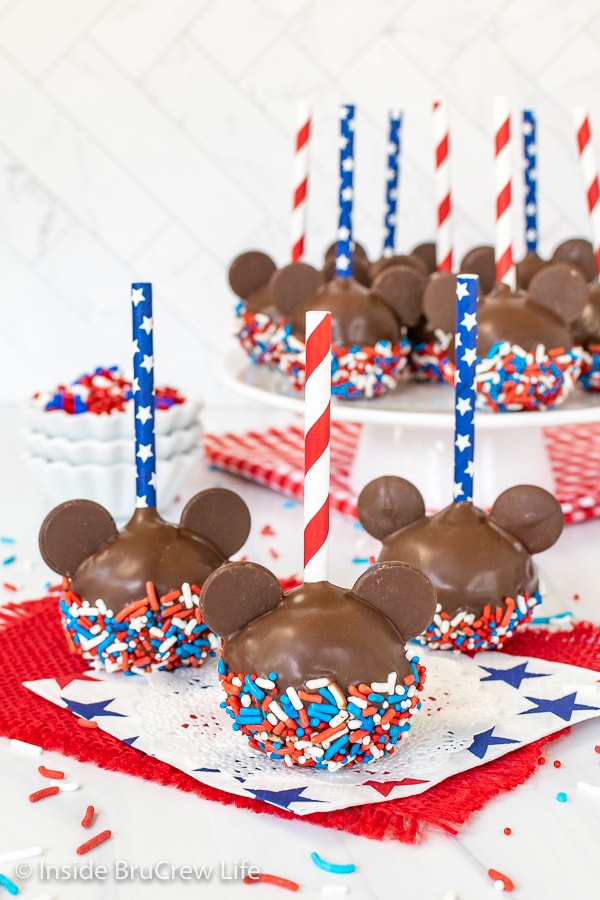 Three Mickey cake pops with red white and blue sprinkles and straws on them.