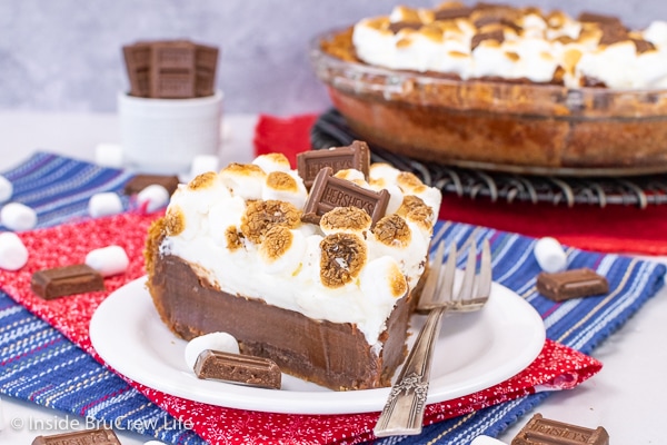 A white plate with a slice of baked s'mores pie topped with toasted marshmallows on it.