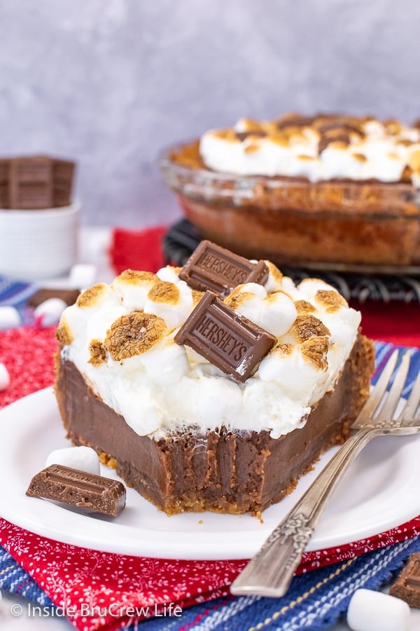 A white plate with a slice of chocolate s'mores pie topped with marshmallow mousse and toasted marshmallows with a bite take out of the pie.