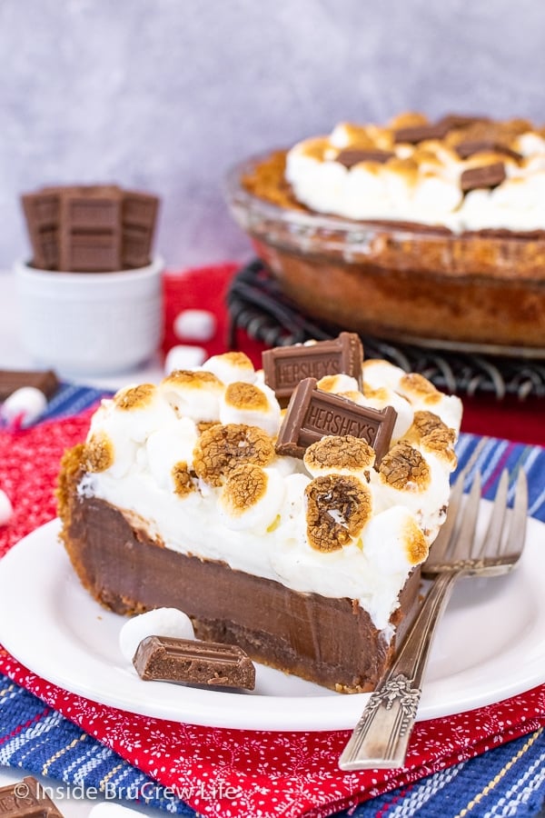 A white plate with a slice of chocolate s'mores pie topped with toasted marshmallows on it.