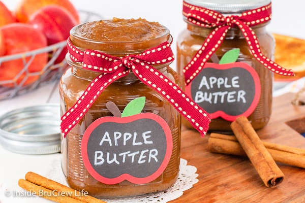 Two clear jars with ribbons and labels filled with homemade apple butter.
