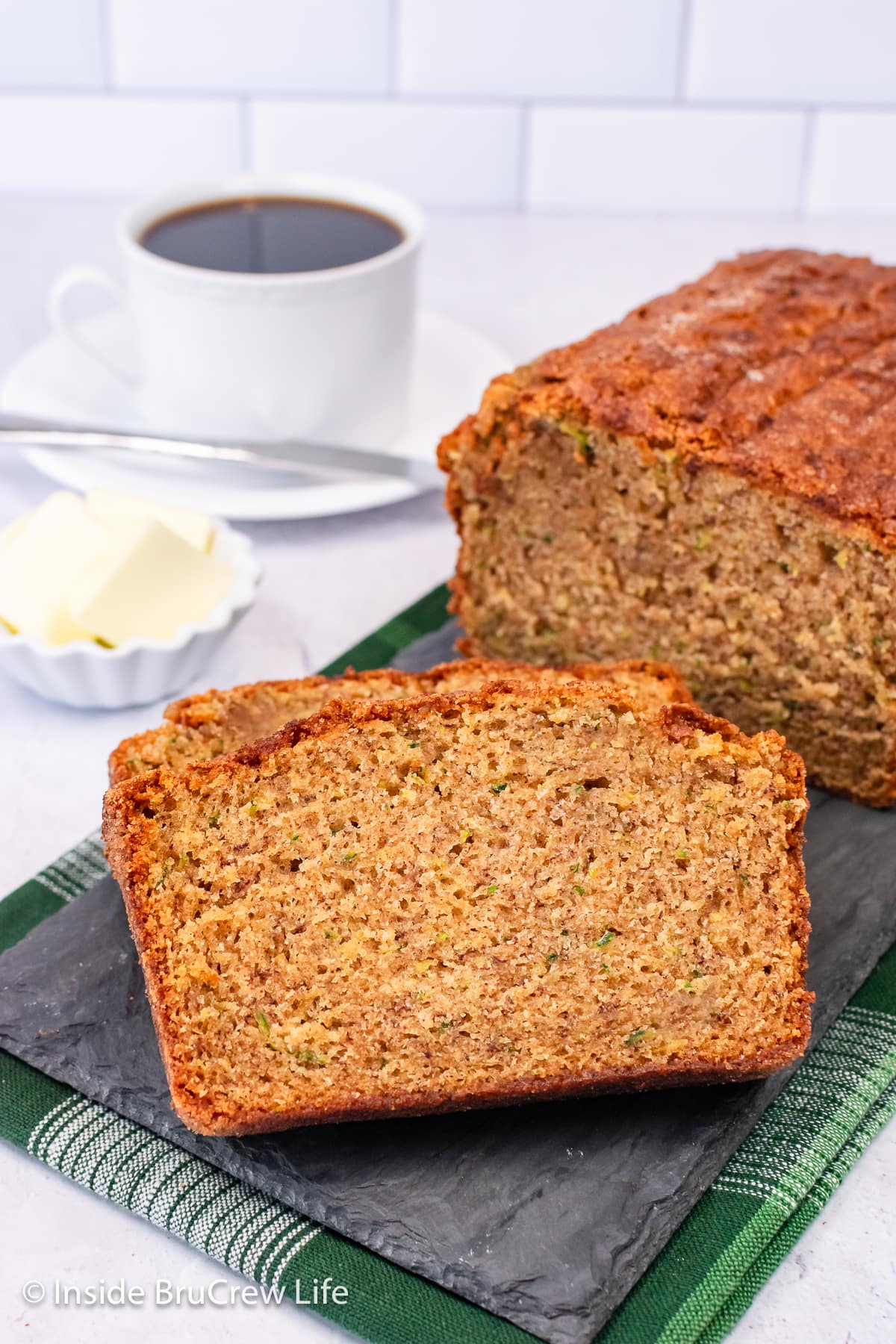 A loaf of zucchini bread with two slices lying beside it.