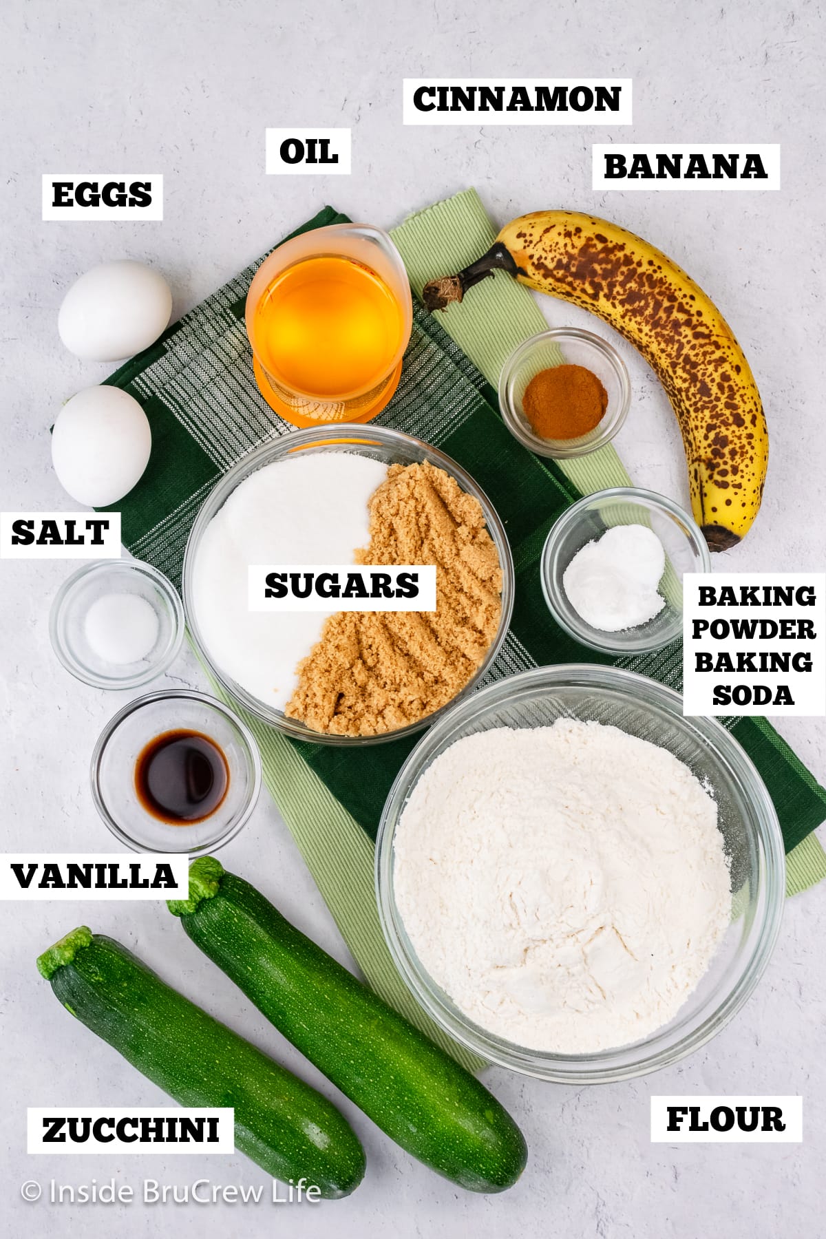 A white board with bowls of ingredients needed to make a sweet bread with zucchini and bananas.