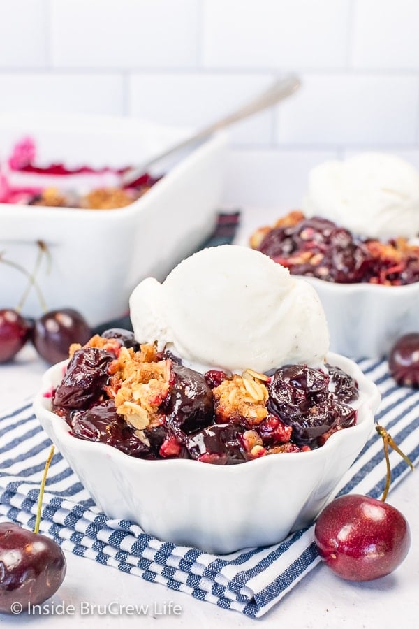 Two white bowls filled with cherry crisp and a scoop of vanilla ice cream.