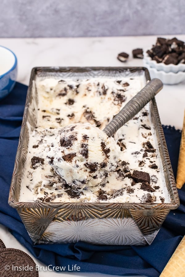 A metal pan filled with cookie cream ice cream and an ice cream scoop sitting on top.