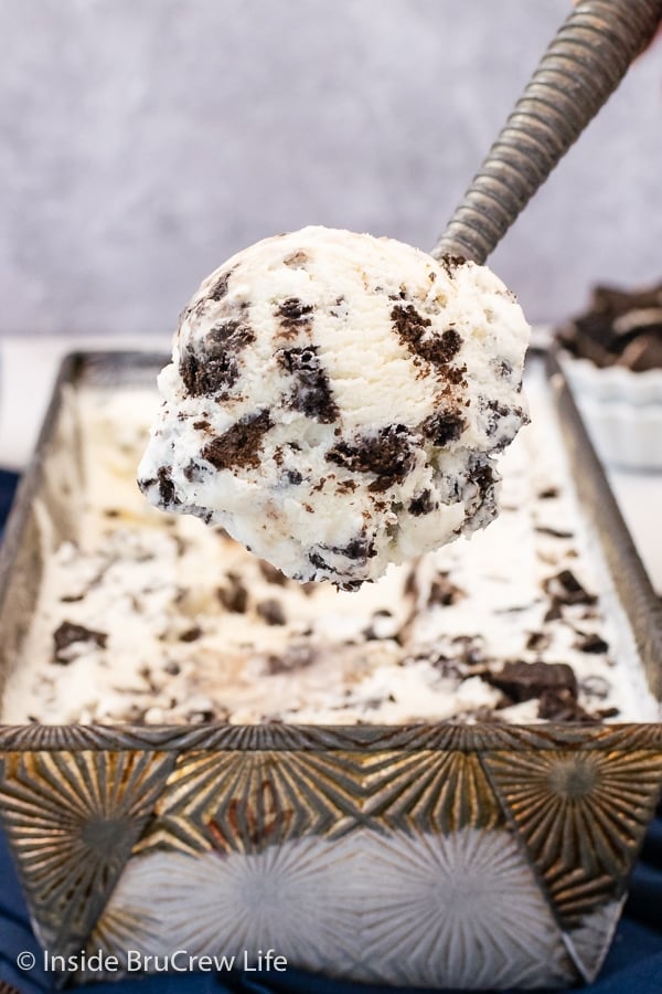 A metal pan filled with Cookies and Cream Ice Cream with an ice cream scoop lifting some out.