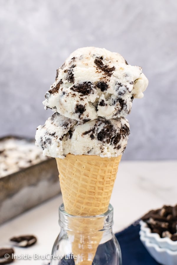 A sugar cone topped with two scoops of cookies n cream ice cream.