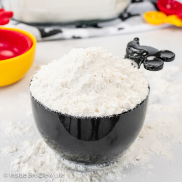 A black measuring cup full of flour.