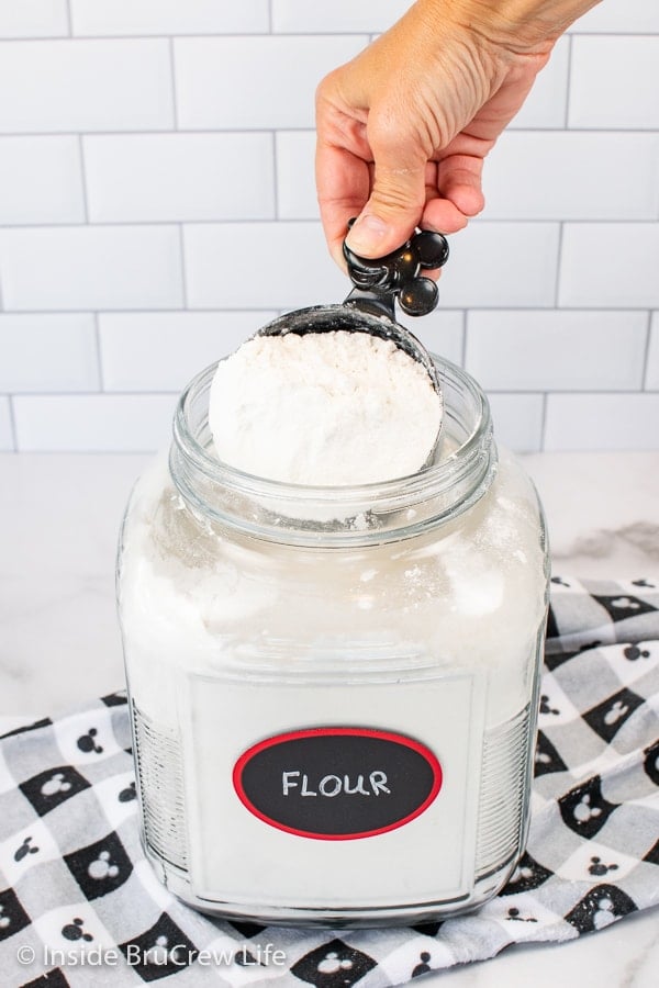 A container of flour with a measuring cup dipping into it to show this is the wrong way to measure flour.