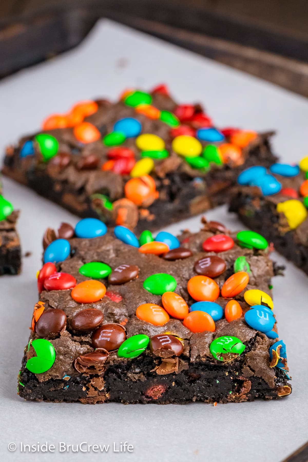 Brownies topped with colorful candies on a paper lined tray.
