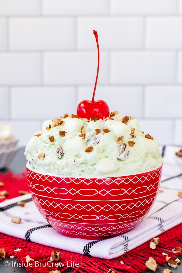 A red bowl filled with green fluff and topped with a red maraschino cherry.
