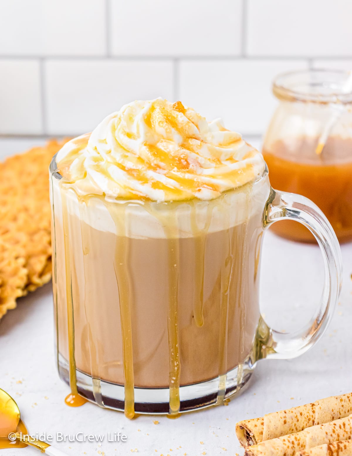 A clear mug with a latte topped with whipped cream in it.