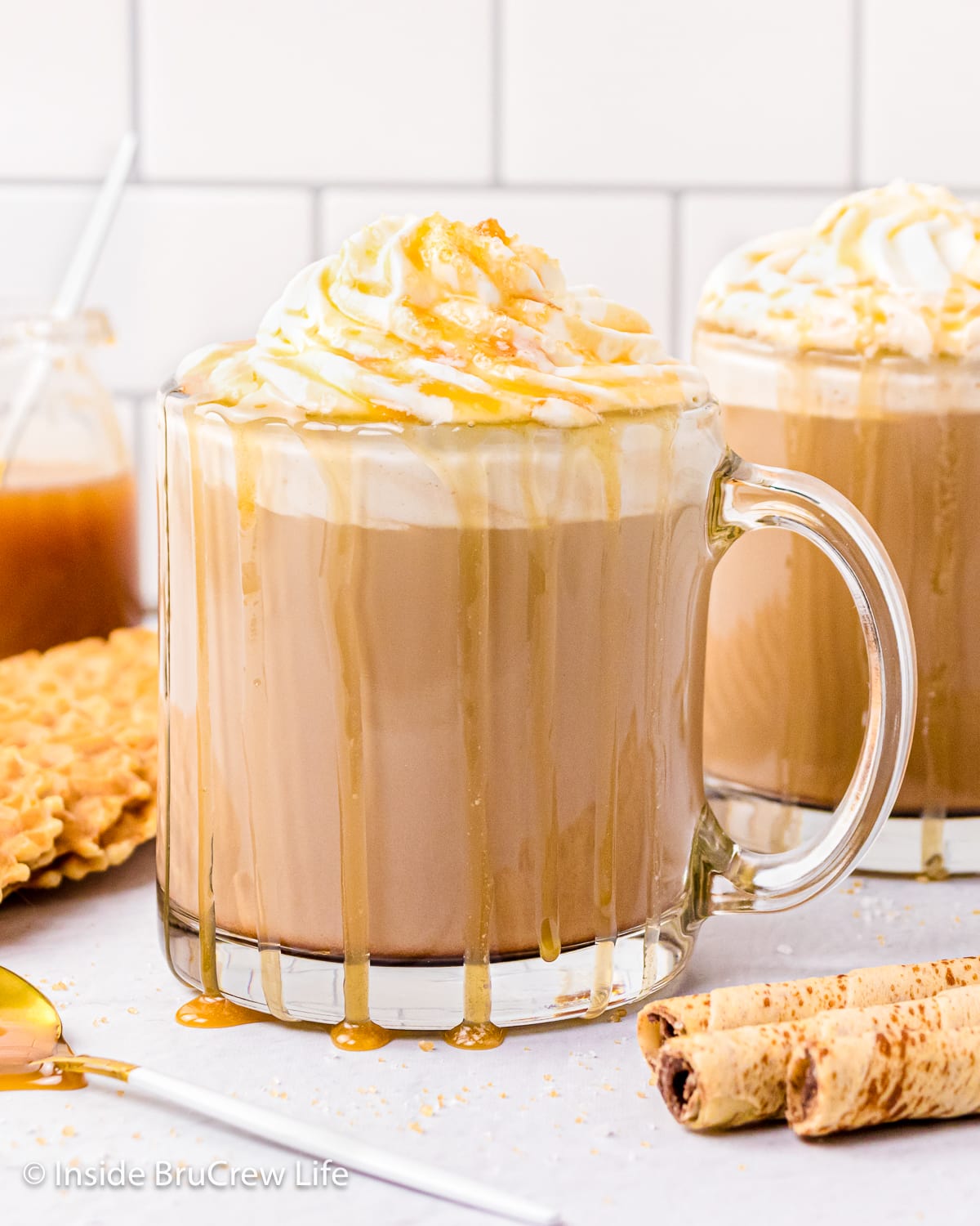 Two clear mugs with hot coffee and whipped cream.