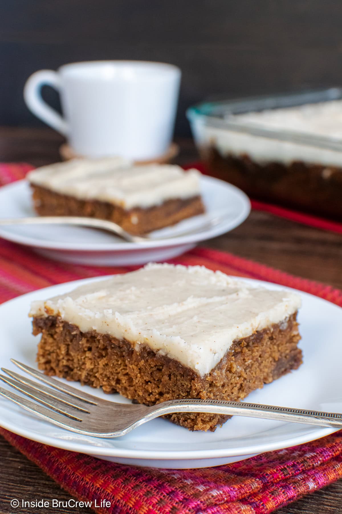 Two white plates with squares of frosted cake on them.