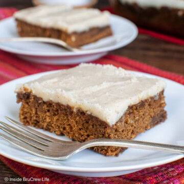 Two white plates with squares of frosted cake on them.