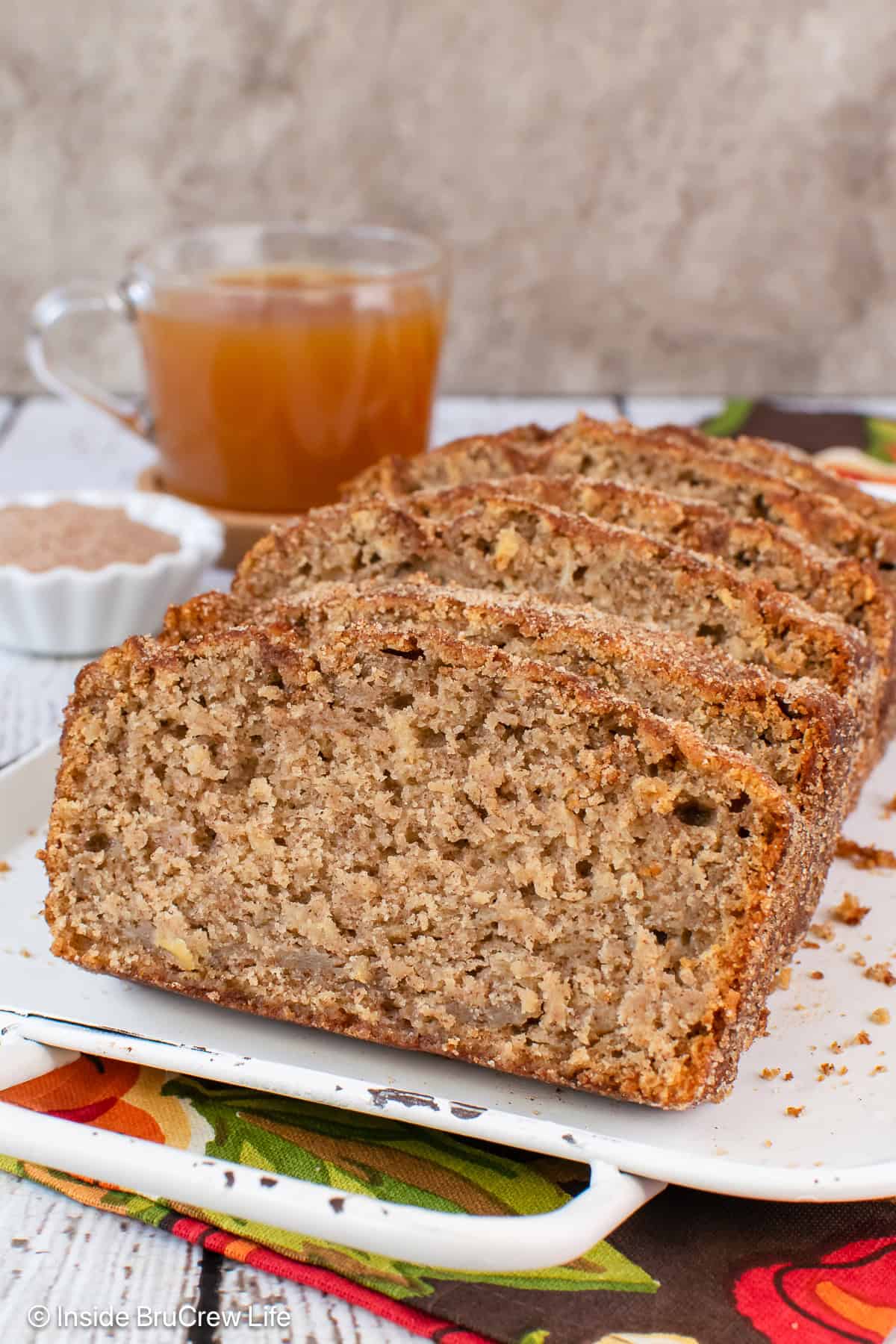 An apple cider bread cut into slices and stacked on a white tray.