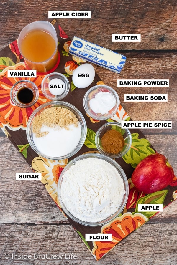 Bowls of ingredients needed to make apple cider bread on a brown board.