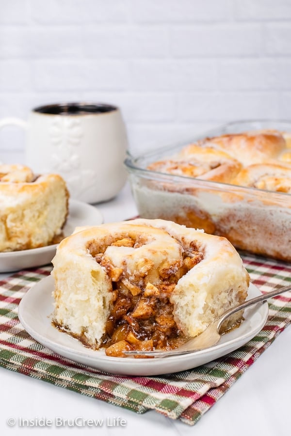 A white plate with apple cinnamon roll with a bite missing out of it.