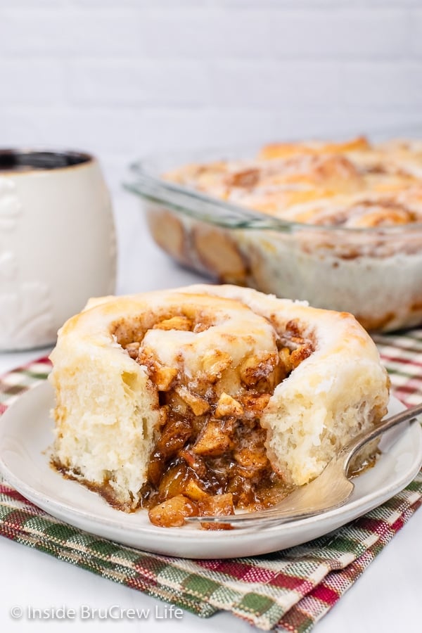 A white plate with a gooey apple cinnamon roll with a bite missing on it.