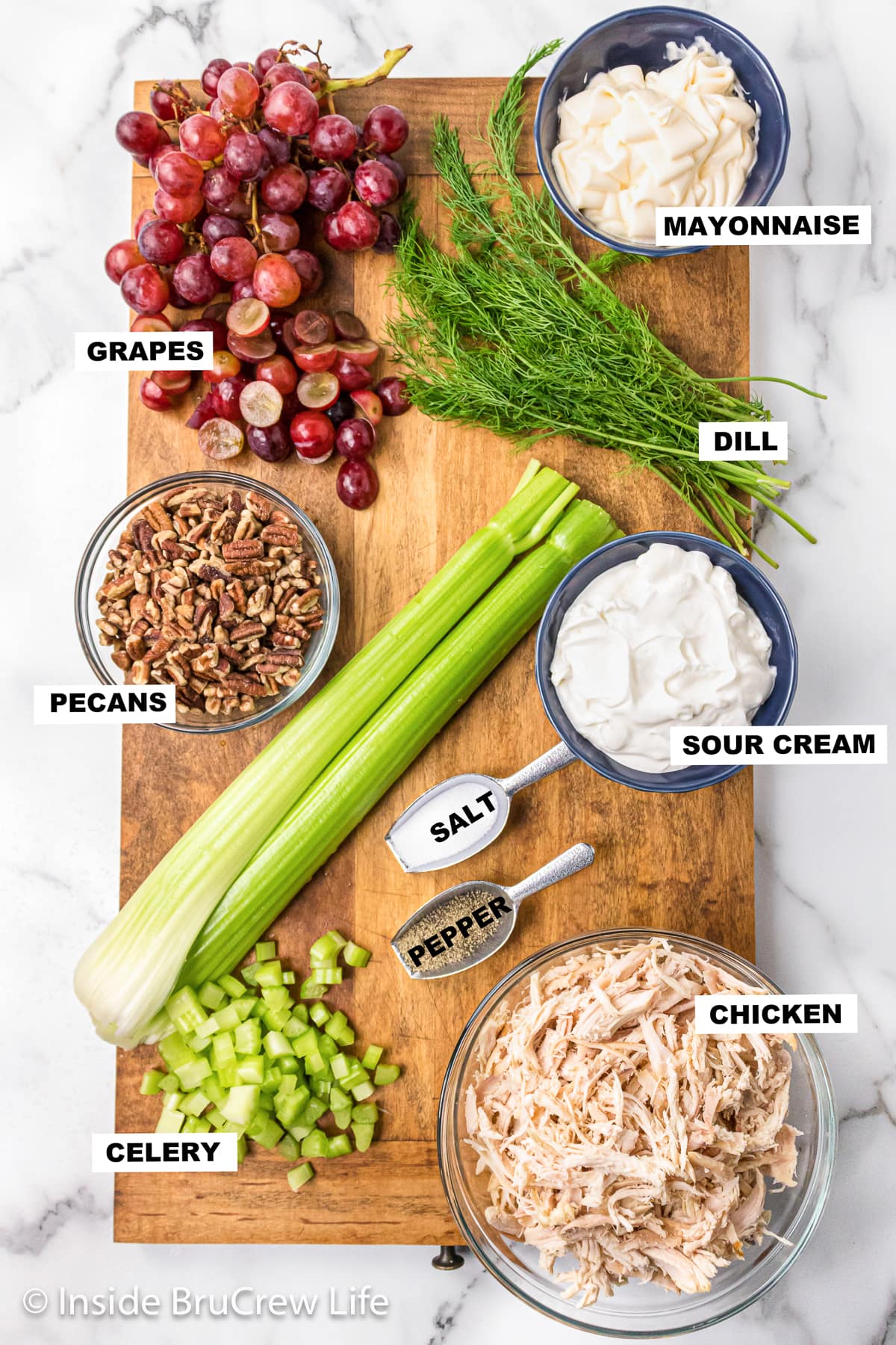 Bowls of ingredients needed to make a chicken salad with dill, grapes, and pecans.