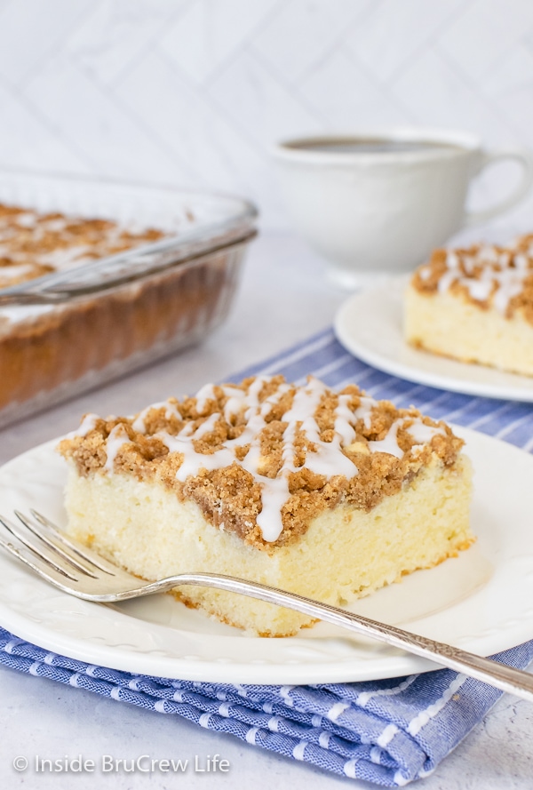 A white plate with a fork and a square of sour cream coffee cake with brown sugar topping and glaze.