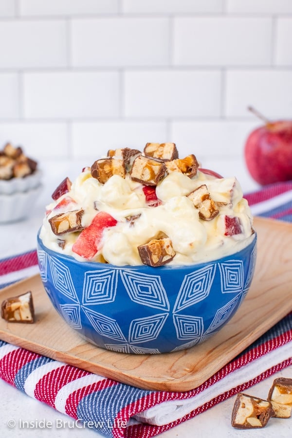 A blue bowl filled with apple snickers salad and topped with extra candy bars.