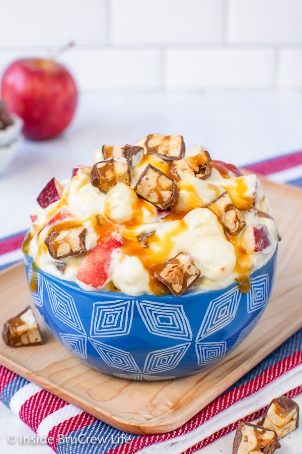 A blue bowl filled with Apple Snickers Salad and drizzled with caramel topping.