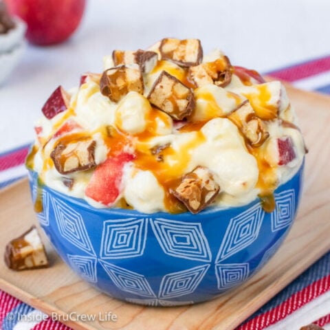 A blue bowl filled with snickers salad and topped with caramel and candy bars.