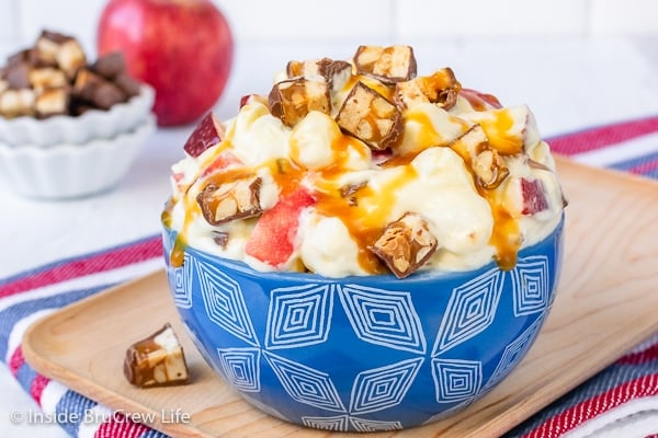 A blue bowl on a wood board filled with apple caramel salad and drizzled with extra caramel.