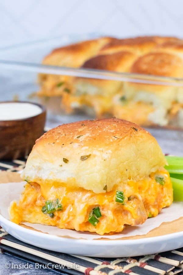 A white plate with a cheesy Buffalo Chicken Slider on it and a pan of sliders behind it.