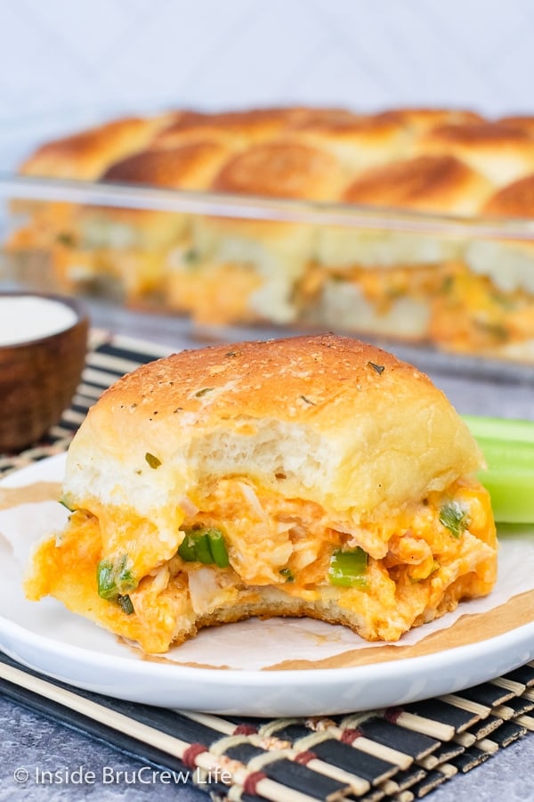 A white plate with a buffalo chicken slider on it with a bite taken out of it showing the cheesy inside.