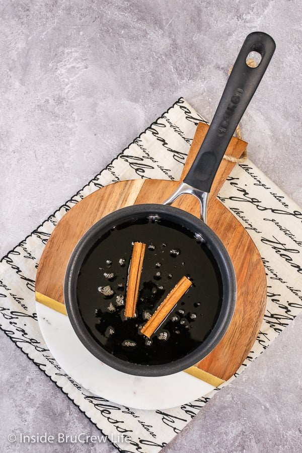 Overhead picture of a saucepan with maple syrup and cinnamon sticks in it.