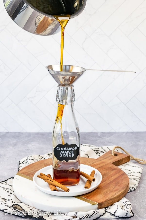 A clear jar being filled with cinnamon maple syrup.