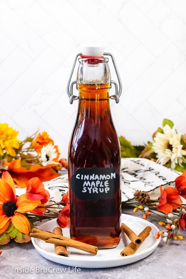 A clear bottle filled with Cinnamon Maple Syrup with a black label on it.