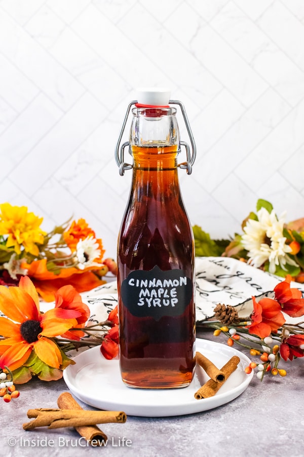 A clear bottle filled with cinnamon maple syrup on a white plate. 