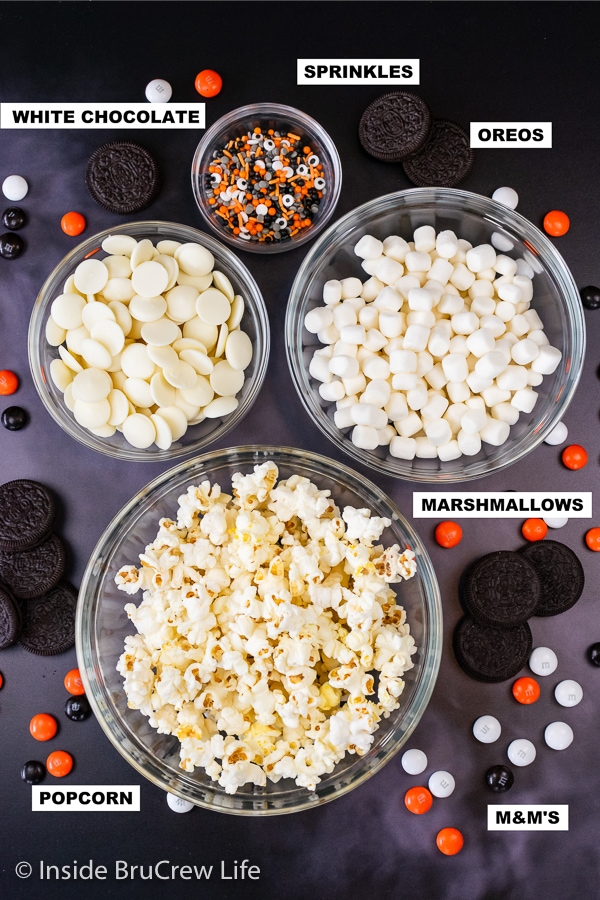 Black background with bowls of ingredients needed to make Halloween popcorn on it.