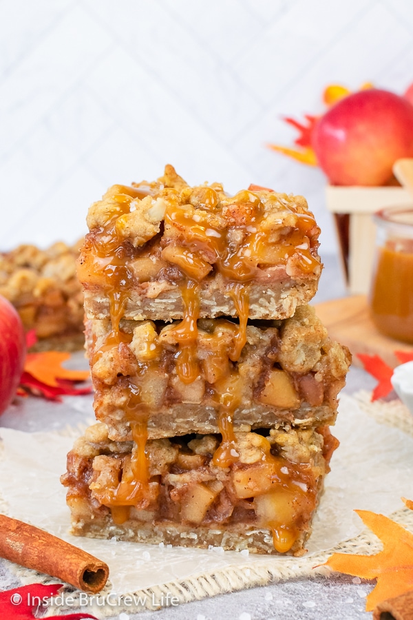 Three apple pie bars stacked on top of each other and drizzled with salted caramel.