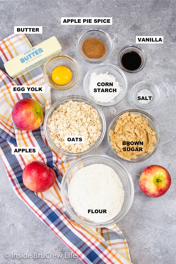 A gray board with bowls of ingredients needed to make salted caramel apple pie bars on it.